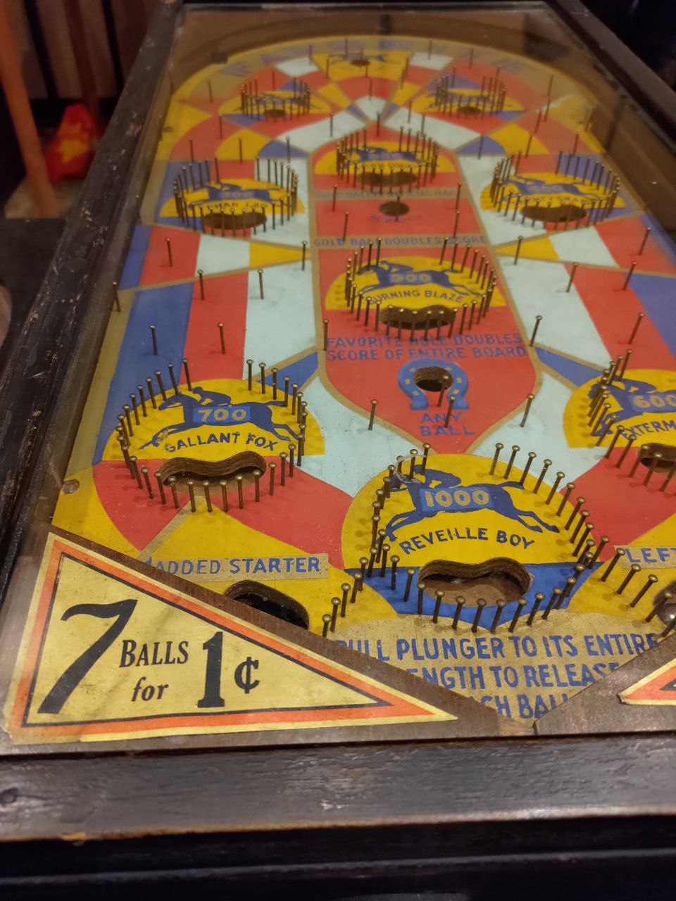 An old pinball machine. It has no flippers, as flippers were not added to pinball until much later. The focus of the image is a vintage sign on the pinball machine advertising 7 balls for only one cent.